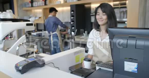 美丽的亚洲女人为一个用非接触式手机支付信用卡系统费用的顾客做外卖咖啡视频的预览图