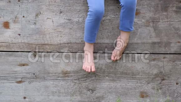 一个小农孩子光着脚坐在木栅栏上视频的预览图