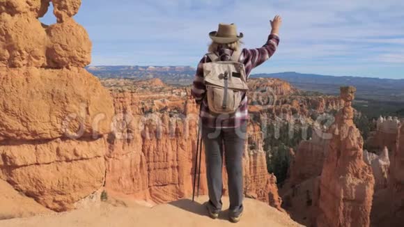 一个徒步旅行者的女人抬起手站在布莱斯峡谷的边缘视频的预览图