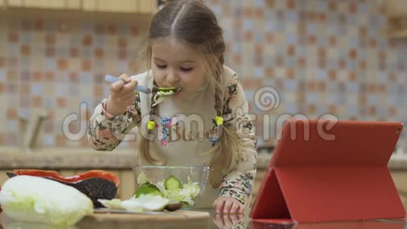 有趣的小女孩尝试了她的第一个煮熟的沙拉并显示拇指在相机视频的预览图