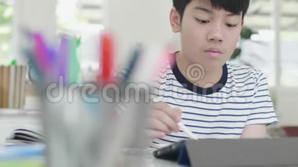 亚洲男孩坐在家里的椅子上做作业用平板电脑找到答案视频的预览图