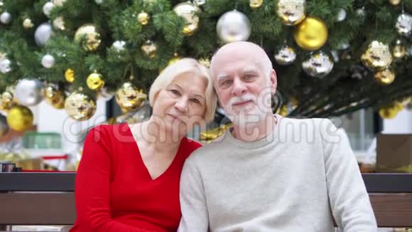 在商场装饰圣诞树附近的老夫妇画像幸福的家庭坐着微笑视频的预览图