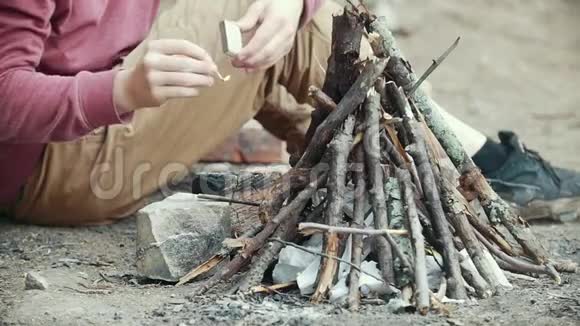 男人手里拿着火柴把树枝放到森林里的小篝火里视频的预览图