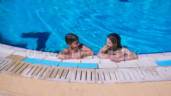 两个孩子在游泳池里喝鸡尾酒放松视频的预览图