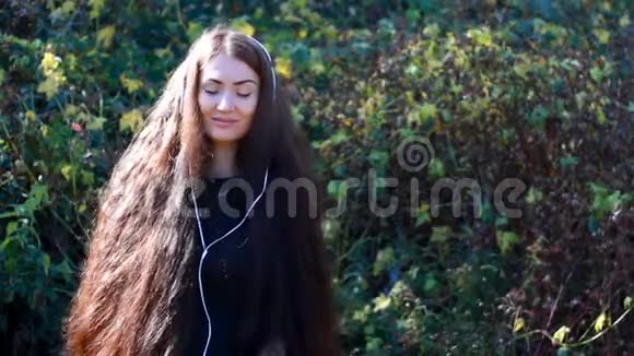 在一个阳光明媚刮风的日子里戴着耳机听音乐的长发的女人视频的预览图