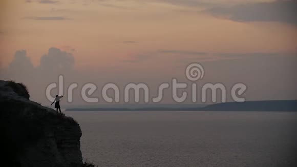 夕阳西下女性的剪影在悬崖边上随风飘扬视频的预览图