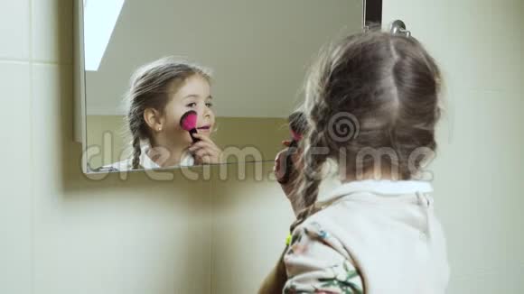 可爱的小女孩在镜子前用刷子把粉末涂在脸上视频的预览图