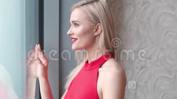 时尚优雅的金发女人在家客厅里穿着红色性感的裙子视频的预览图