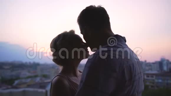 一对欣赏美丽的粉红色日落的夫妇轻轻地笼罩着他们从屋顶眺望视频的预览图