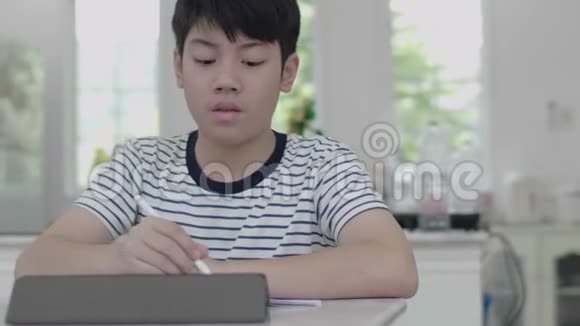 亚洲男孩坐在家里的椅子上用平板电脑做作业找出答案视频的预览图