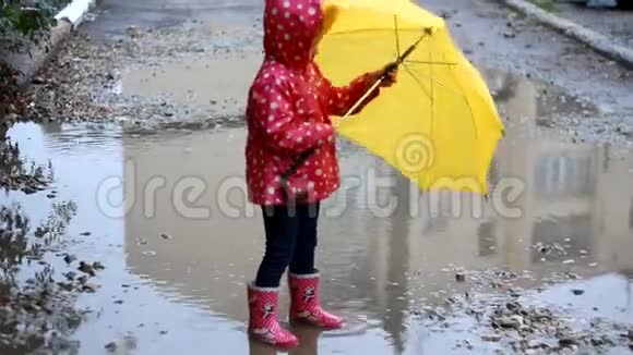 小女孩在雨天的水坑里跳着在伞下玩耍视频的预览图
