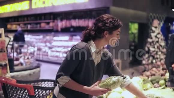 年轻漂亮的黑发女孩在她20的时候在摘那帕甘蓝和花椰菜把它们放进购物车视频的预览图