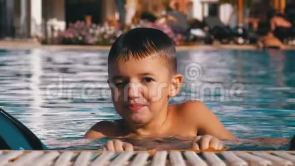 快乐男孩与拖鞋游泳在一个游泳池与蓝水慢动作视频的预览图