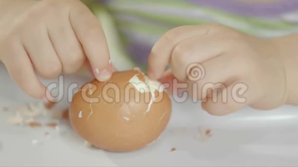 一个小女孩坐在一个儿童椅子上用一个煮熟的鸡蛋清理外壳并吃掉它视频的预览图