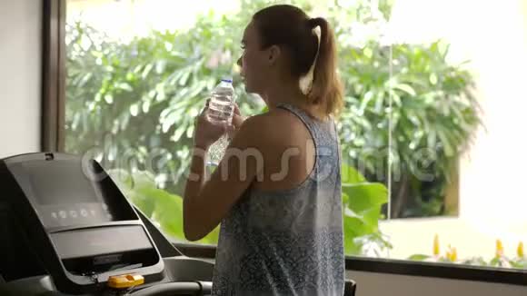 漂亮的白种人女孩在运动健身房里喝水和跑步慢动作3840x2160视频的预览图