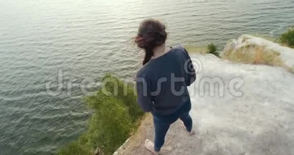 日出时年轻女子在悬崖边热身的后景视频的预览图