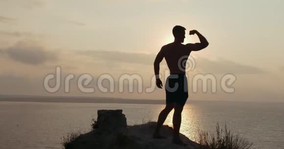 日出时在岩石悬崖上做早操的肌肉男剪影视频的预览图