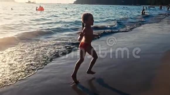 一个赤脚的小女孩在晚阳的温暖光线下沿着大海在潮湿的沙子上奔跑的缓慢运动粗心和粗心视频的预览图