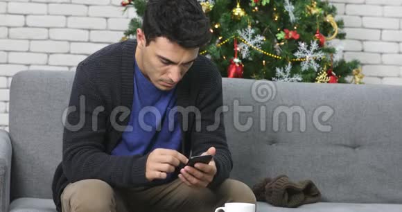 高加索男人在沙发上用智能手机视频的预览图