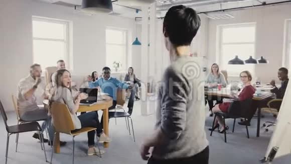 镜头跟随快乐的亚洲男人做滑稽的胜利庆祝舞蹈走在办公室同事鼓掌笑4K视频的预览图