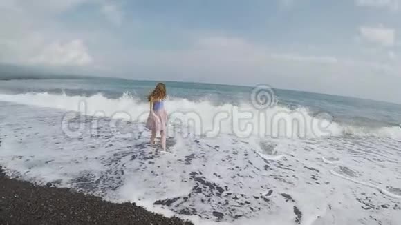 海浪拍岸而下黑色沙滩上的女孩身上飞舞着巨大的浪花视频的预览图