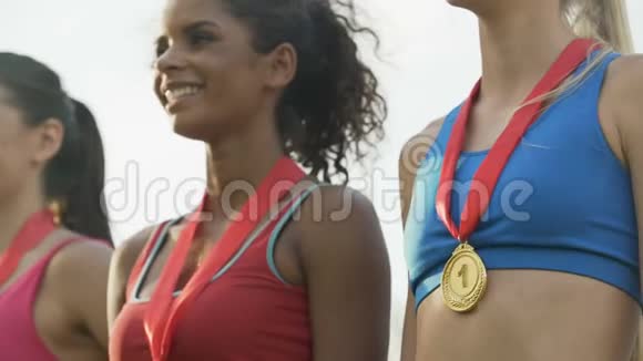 欢乐的多种族女孩站在领奖台上自豪地在胸前展示奖牌视频的预览图