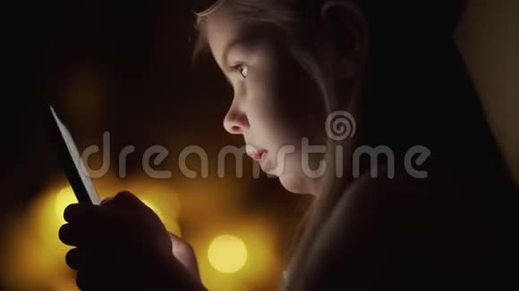 可爱的小女孩晚上使用智能手机背景灯视频的预览图