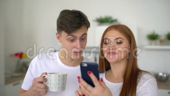 快乐的一对夫妇在家厨房早餐时使用智能手机一起浏览在线享受着喝咖啡的乐趣4千克视频的预览图