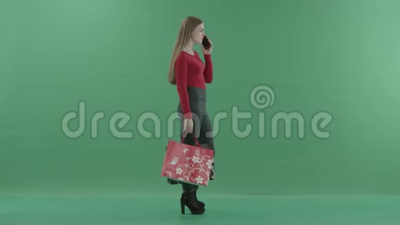 穿着休闲服的漂亮女人拿着购物袋在手机上说话她站在工作室里视频的预览图