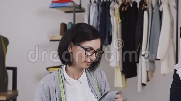 一个裁缝坐在桌子旁用剪刀从灰色的材料中剪出图案用来缝制衣服视频的预览图