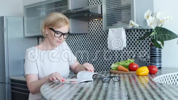女人坐在餐桌旁的厨房里正在看一道菜的菜谱视频的预览图