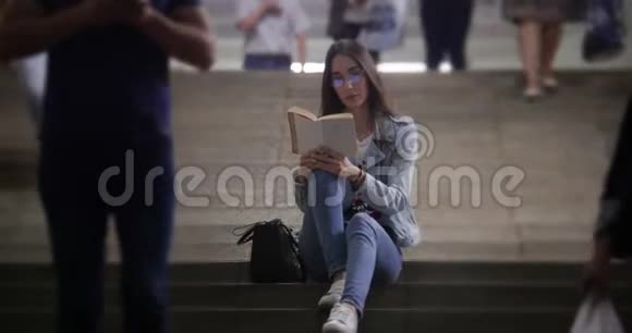 坐在地铁楼梯上看书的年轻女子视频的预览图