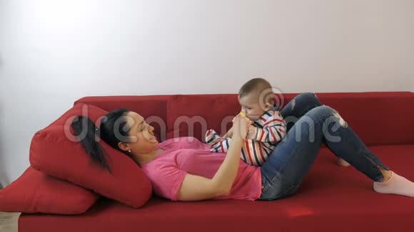 妈妈把婴儿的脚放在沙发上玩视频的预览图