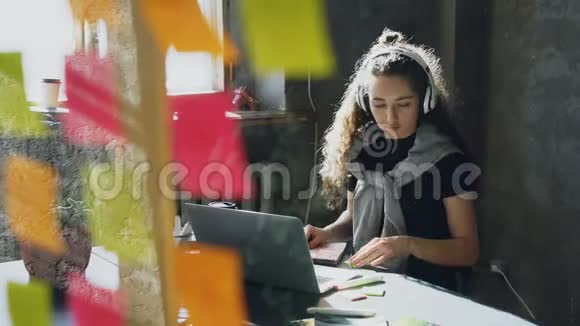 富有创造力的年轻女商人戴着耳机边听音乐边用笔记本电脑在办公桌上跳舞唱歌视频的预览图