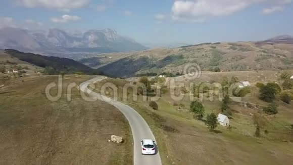 无人驾驶飞机飞过修补过的两条车道白色汽车穿过黑山山和岩石的田野视频的预览图