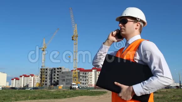 戴着黑色眼镜的检查员拿着一台笔记本电脑在建筑背景下用电话交谈视频的预览图