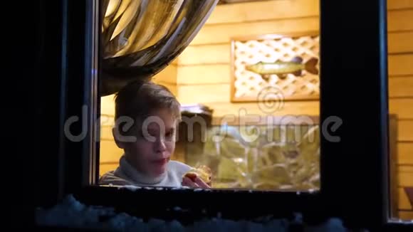 冬天的夜晚在靠近窗户的温暖明亮的房间里站着一个年轻人在户外射击视频的预览图