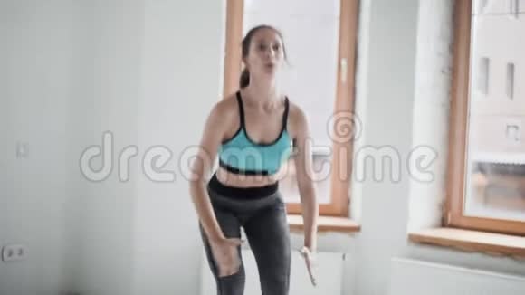 穿着运动服的年轻黑发女孩在明亮的房间里做运动在家做运动健康的生活方式蹲视频的预览图