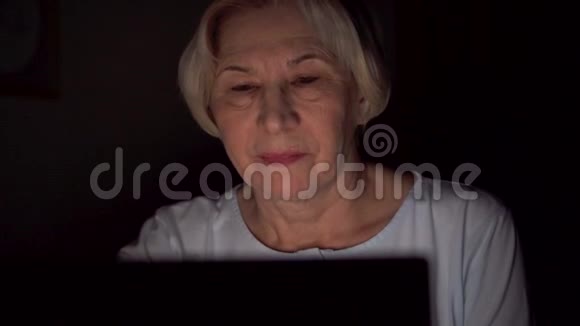 老妇人在家中休息深夜用笔记本电脑阅读新闻只有一张漆黑的脸视频的预览图