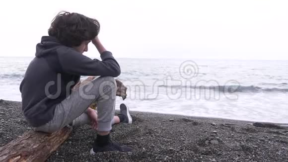 一个孤独的男孩坐在岸上向大海扔石头4k慢动作视频的预览图