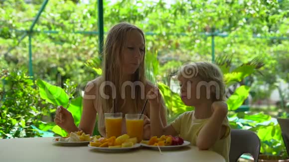 一位年轻女子和她儿子在热带花园吃水果晚餐时的慢镜头视频的预览图