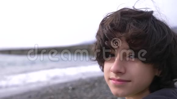 一个可爱的少年卷发在大海的背景下4k慢动作视频的预览图