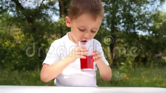 一个快乐的孩子在大自然的背景下从玻璃杯中喝浆果汁视频的预览图