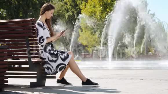 穿着连衣裙的年轻女商人坐在长凳上在写字板上讲话视频的预览图