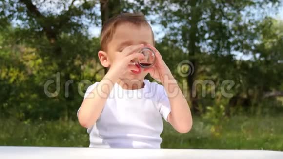 一个快乐的孩子在大自然的背景下用玻璃杯子喝浆果汁视频的预览图