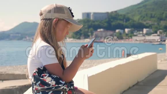 夏天小女孩在海边的堤岸上坐着手机儿童控制智能手机视频的预览图