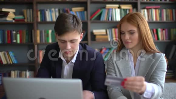 年轻的微笑夫妇坐在沙发上用笔记本电脑和信用卡在互联网上购买4k男子和妇女视频的预览图