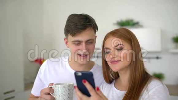 快乐的一对夫妇在家厨房吃早餐一起使用智能手机上网浏览快乐夫妻使用智能手机视频的预览图