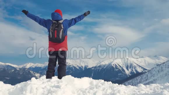 男子背着背包站在雪山顶上胜利者摆姿势举起双手欣赏风景和成就视频的预览图