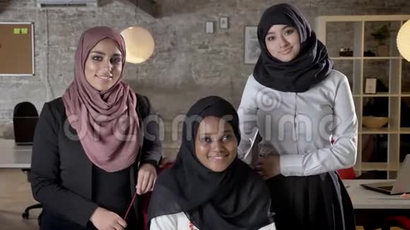 三位年轻的穆斯林妇女戴着头巾在现代办公室里面带微笑地看着镜头视频的预览图